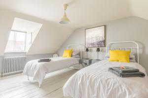 two beds in a white room with yellow accents at White Cottage in Whitstable