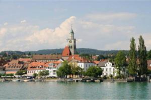 a building with a clock tower next to a body of water at Neue Bodenseeferienwohnung mit Terrasse und Garten in Uhldingen-Mühlhofen