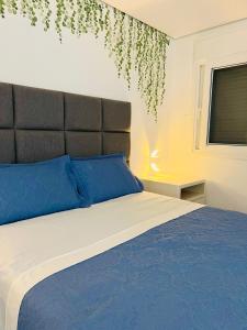 a bedroom with a bed with blue pillows and a window at Apartamento a 100 m da praia in Juquei
