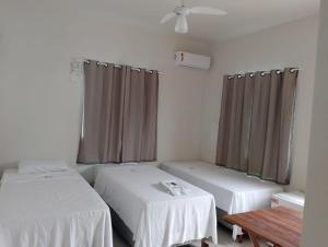 Habitación con 2 camas, mesa y cortinas en Anexo Canadense - Pousada Mineira SJB, en São João da Barra