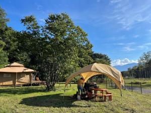 Un uomo in piedi sotto una tenda in un campo di Camp inn Kiyosato GRANDEUR - Vacation STAY 42081v a Hokuto