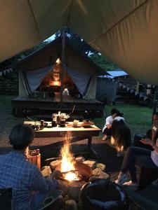 Un gruppo di persone seduti intorno al fuoco in una tenda di Camp inn Kiyosato GRANDEUR - Vacation STAY 42080v a Hokuto