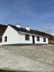 een wit gebouw met zwarte ramen en een oprit bij Eileen’s Cottage in Donegal
