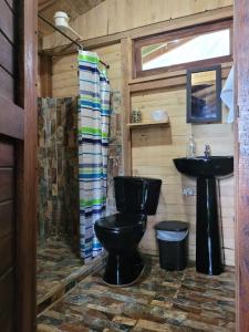 a bathroom with a black toilet and a sink at Cabaña en Medio del Bosque con Jacuzzi - Santa Elena in Santa Elena