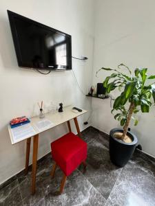 una scrivania con sedia rossa e una TV a parete di Linda Kitnet mobiliada a São Vicente
