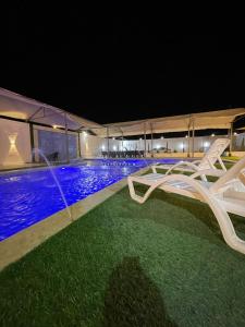 una piscina notturna con due sedie a sdraio bianche di شالية ومزرعة ضوء القمر a Umm el ‘Amad