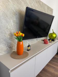 an orange vase with orange flowers on a white tv stand at Center apartment in Gjilan