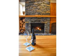a bottle of wine and glasses on a table in front of a fireplace at River Birches in Turangi
