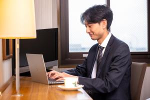 een man in een pak die aan een bureau zit met een laptop bij City Hotel Air Port in Prince in Izumi-Sano