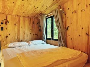 Bett in einem Holzzimmer mit Fenster in der Unterkunft XOM Organic Farm Stay in Pleiku