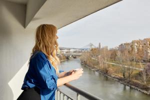 URBAN ISLAND I Riverside Apartments في فيينا: امرأة تقف على شرفة تطل على نهر
