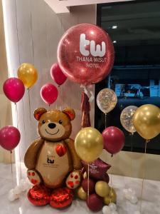 un oso de peluche sentado al lado de un montón de globos en Thana Wisut Hotel - SHA Plus, en Bangkok