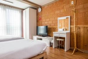 a bedroom with a bed and a desk with a television at Red Clay Pension in Jeju