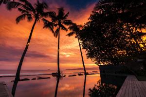 zachód słońca nad oceanem z palmami i basenem w obiekcie Villa Manis Beachfront Candidasa w mieście Candidasa