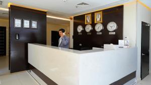 un homme debout derrière un comptoir avec des horloges sur le mur dans l'établissement Saray Hotel Apartments, à Koweït