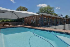 a swimming pool with an umbrella next to a building at Cadman Motor Inn and Apartments in Tamworth