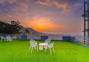 a group of chairs and a table on a balcony with a sunset at Kanavu Valley View Premium 4 Star Resort Ooty by VOYE HOMES in Ooty