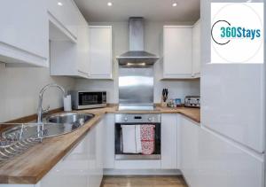 Luxury 1 Bedroom Apartment 06 with Parking in Maidenhead by 360stays في ميدينهيد: مطبخ مع دواليب بيضاء ومغسلة