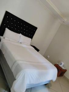 a bedroom with a white bed with a black headboard at Rest Camp Lodge in Manzini