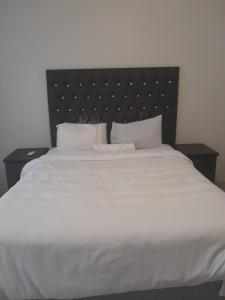 a large white bed with a black headboard and white pillows at Rest Camp Lodge in Manzini