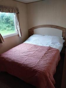 Norfolk broads caravan sleeps 8 في Belton: غرفة نوم بسرير وبطانية حمراء ونافذة