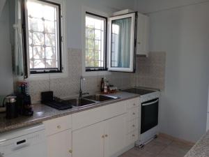 a kitchen with white cabinets and a sink and two windows at Villa Santa Marina in Spetses