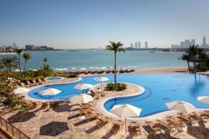 a pool with chairs and umbrellas next to a beach at Tiara Residences, Free beach & pool access in Dubai