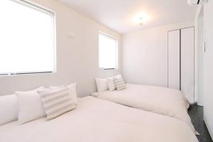 two beds in a white room with two windows at bHOTEL Komachi - Apt for 6ppl few mins walk to Peace Park in Hiroshima