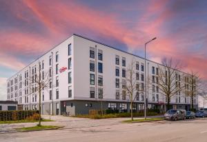 un bâtiment blanc avec des voitures garées dans un parking dans l'établissement Ramada Encore by Wyndham Munich Messe, à Munich