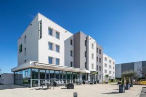 un bâtiment blanc avec des tables et des chaises devant lui dans l'établissement B&B HOTEL Lyon Aéroport Saint-Quentin-Fallavier, à Saint-Quentin-Fallavier