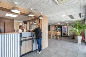 a woman standing at a counter in a restaurant at B&B HOTEL Lyon Aéroport Saint-Quentin-Fallavier in Saint-Quentin-Fallavier