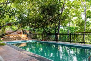 a swimming pool with a black fence and trees at Trance rabara resort in Avissawella