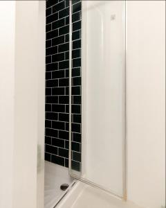 prysznic ze szklanymi drzwiami i ścianą wyłożoną czarnymi kafelkami w obiekcie Primrose Hill Charming 1-Bed Flat w Londynie