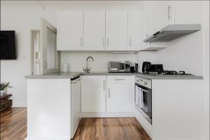una cucina bianca con armadietti bianchi ed elettrodomestici in acciaio inossidabile di Primrose Hill Charming 1-Bed Flat a Londra