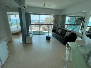 uma sala de estar com um sofá preto e janelas grandes em מלון דירות אוקיינוס במרינה דירות עם נוף לים em Herzliyya B