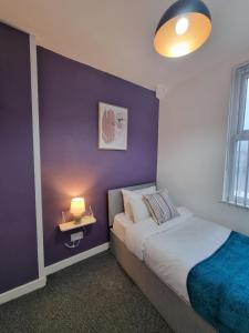 a bedroom with a purple wall with a bed and a lamp at Spacious 3 bedroom house near city centre & docks/free parking in Liverpool