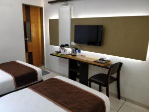 a hotel room with two beds and a desk with a television at Hotel Royal Shelter Vapi in Vapi