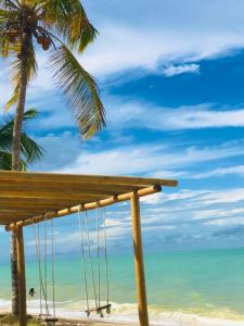 a wooden bench sitting on the beach with a palm tree at Pousada Praia Do Farol in Alcobaça