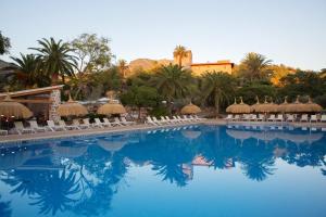 a swimming pool with chairs and palm trees and a building at Hotel Es Port in Port de Soller