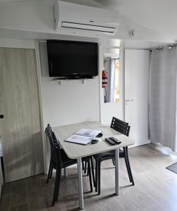 a dining room table with chairs and a tv on the wall at Mobil Home (Clim, TV)- Camping Falaise Narbonne-Plage 4* - 003 in Narbonne-Plage