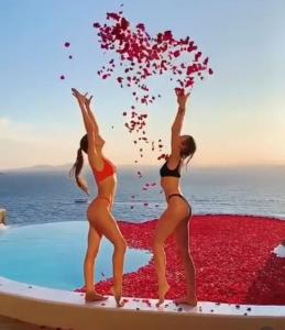 duas mulheres em fatos de banho de pé numa prancha de surf com flores em Cavo Tagoo Mykonos em Míconos