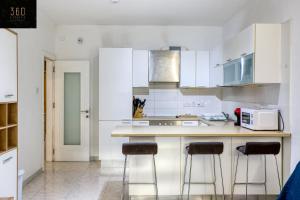 una cucina con armadi bianchi e 2 sgabelli da bar di Spacious, central APT in Paceville/St Julians by 360 Estates a San Giuliano