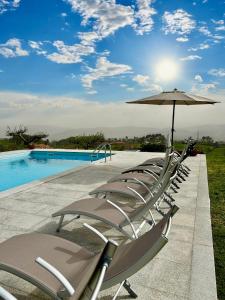 eine Reihe von Stühlen mit einem Sonnenschirm und einem Pool in der Unterkunft Matos Casas de Campo in Cabeceiras de Basto