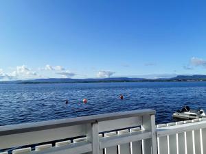 a boat in the water next to a white fence at Flaskebekk at Nesodden with unbeatable Oslo Fjord views and a private beach hut in Nesoddtangen