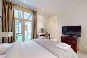 - une chambre avec un grand lit et une télévision à écran plat dans l'établissement Stunning 2BD flat in South Kensington with a patio, à Londres