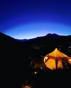 une tente éclairée assise sur une colline la nuit dans l'établissement @alasaguas, à San José de Maipo