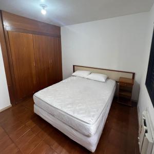 グアルジャにあるAPARTFLAT Pitangueiras a 3 minutos da praia!の白いベッドと木製キャビネット付きのベッドルーム1室