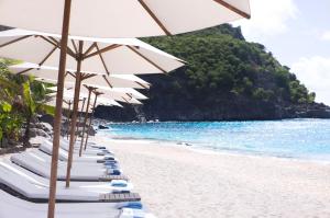 a row of beach chairs with umbrellas on a beach at Hôtel Barrière Le Carl Gustaf St Barth in Gustavia