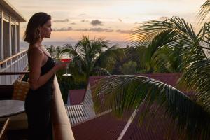 une femme debout sur un balcon avec un verre de vin dans l'établissement Hôtel Barrière Le Carl Gustaf St Barth, à Gustavia