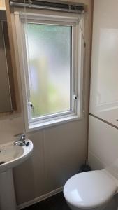 a bathroom with a toilet and a sink and a window at Cosy 3-Bed hot tub Lodge in Pr3 in Preston